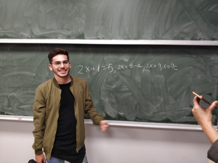 A smiling young man next to a blackboard with equations