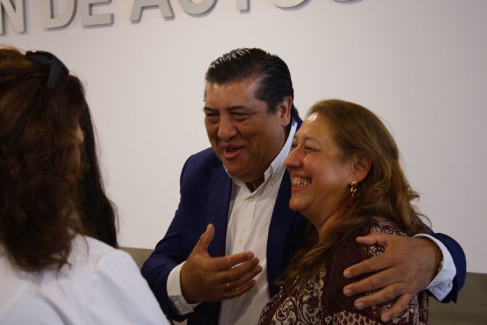 A man and a woman laughing arm in arm in front of the conference mural