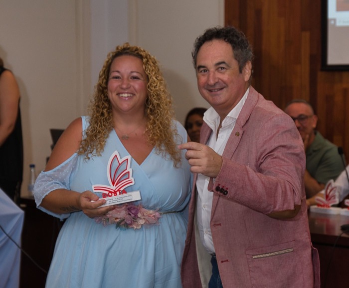 A curly-haired woman laughing with her Dosta Awards trophy